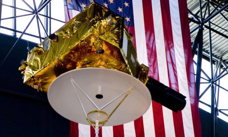 Close-up of a gold and white Pioneer 10 spacecraft model displayed against an American flag.