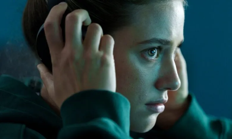 Close-up of a young woman adjusting headphones, bathed in cool blue light, a pensive expression on her face.