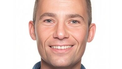 Smiling man with short brown hair wearing a blue shirt against a white background.