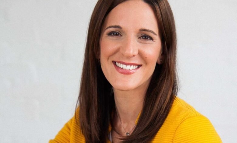 Smiling woman with brown hair wearing a yellow jacket.