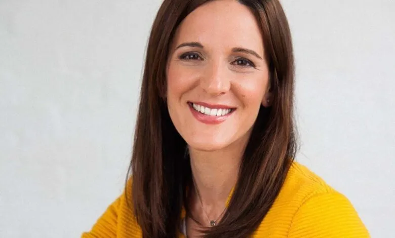 Smiling woman with brown hair wearing a yellow jacket.