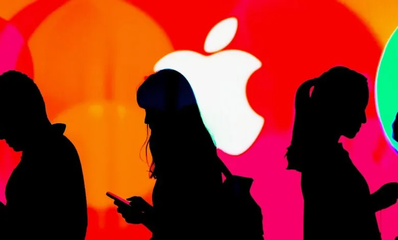 Silhouettes of people using smartphones against a vibrant background featuring the Apple logo.