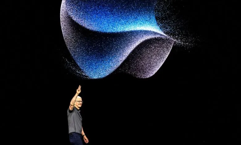 Tim Cook, Apple CEO, gestures on stage during a product launch event, with a dynamic blue and purple particle effect above him.