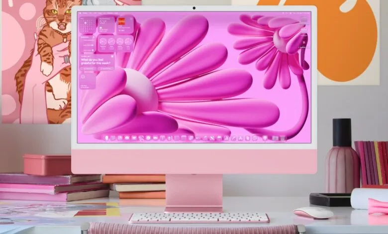 Pink Apple iMac displaying a vibrant pink floral wallpaper. A matching keyboard and mouse are on the desk.