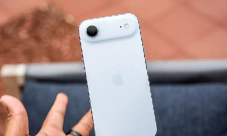 Close-up of a person holding a light blue iPhone 14, showcasing its rear camera and Apple logo.