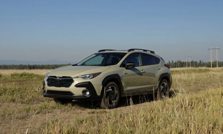 A light tan Subaru Crosstrek Hybrid parked in a dry, grassy field under a clear blue sky.