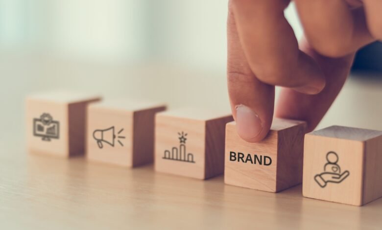 Hand placing a wooden block with the word 'BRAND' among other blocks showing marketing icons.