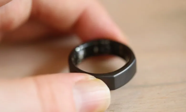 Close-up of a person's thumb and finger holding a sleek, black smart ring.