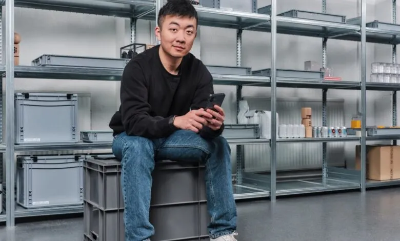 Carl Pei, CEO of Nothing, sits in a warehouse, looking at his phone.