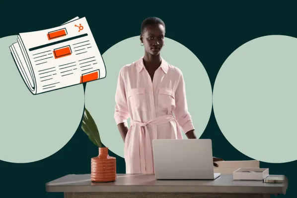 Woman in pink dress standing at a desk with a laptop and a newspaper illustration.