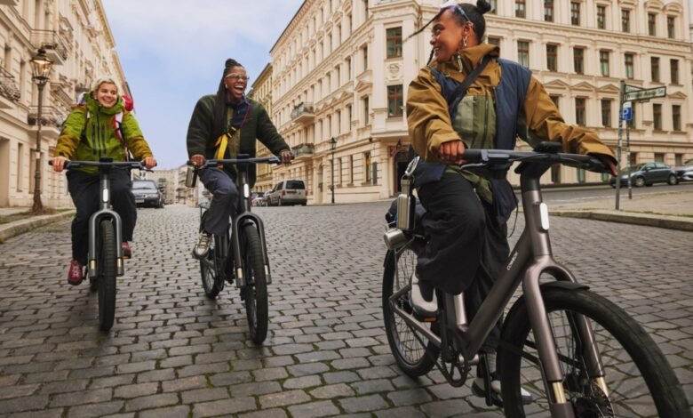 Three friends enjoy a bike ride through a cobblestone street in Berlin, Germany, on stylish e-bikes.