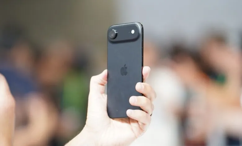 Close-up of a hand holding a black iPhone, showcasing its rear camera and Apple logo.