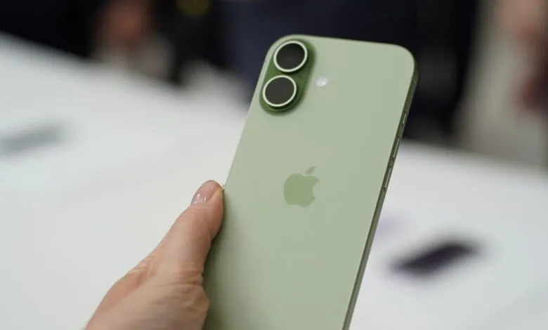 Close-up of a person holding a pale green iPhone, showcasing its dual-lens camera and Apple logo.