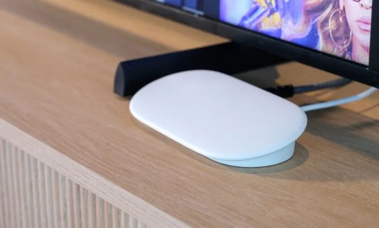 White streaming device connected to a TV on a light wood surface.