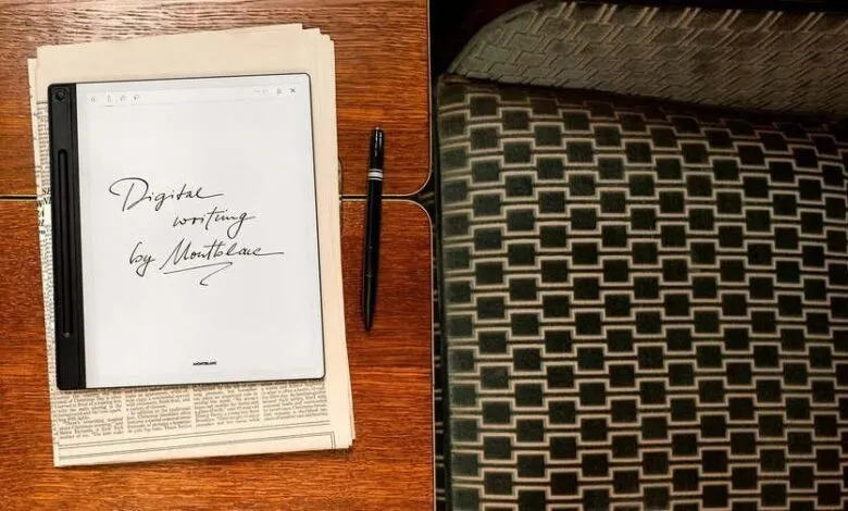 Montblanc digital writing pad on a wooden desk with a pen, next to a patterned chair.