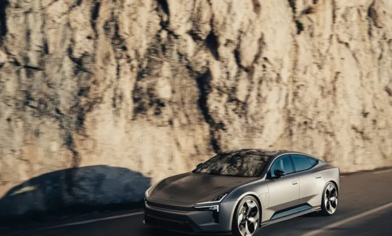 Sleek, silver electric car driving along a road next to a rocky cliff.