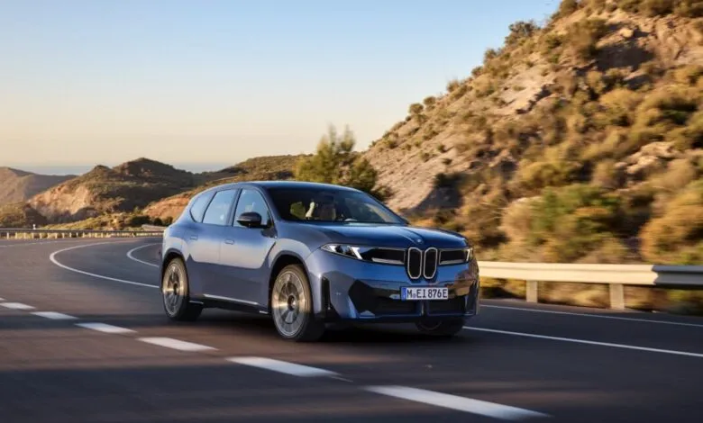 Blue BMW iX3 electric SUV driving on a scenic coastal road.
