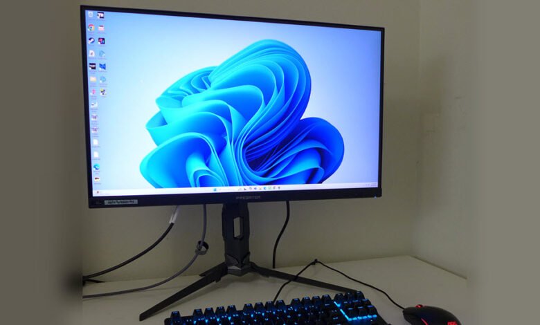 A computer monitor displaying the Windows 11 wallpaper, with a keyboard and mouse in the foreground.