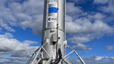 Close-up of a silver rocket against a blue sky with fluffy white clouds. The rocket displays the European Union and ESA logos.