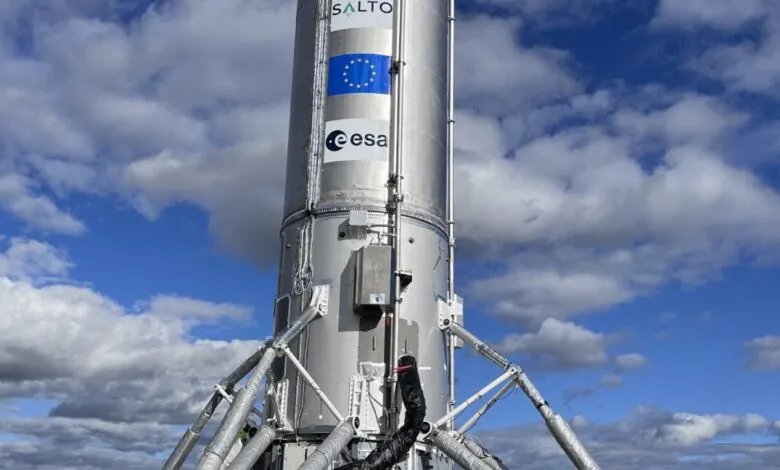 Close-up of a silver rocket against a blue sky with fluffy white clouds. The rocket displays the European Union and ESA logos.