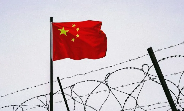 Chinese flag flies near barbed wire fence.