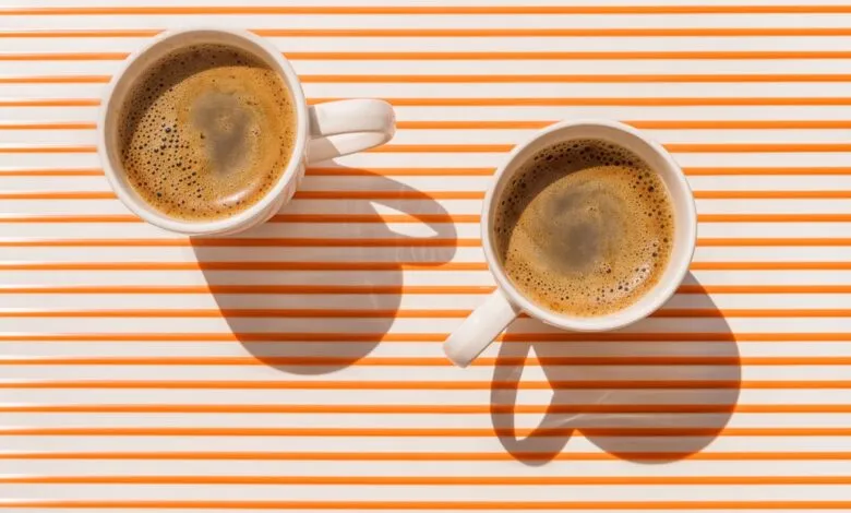 Two cups of coffee on a striped orange and white surface, bathed in sunlight.