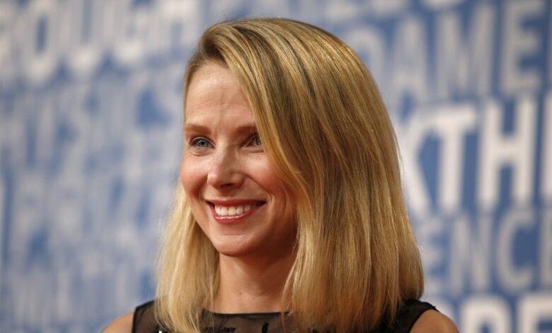 Marissa Mayer smiles at an event with a blurred blue background.