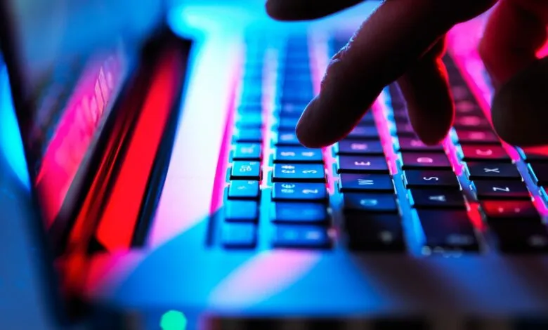 Close-up of hands typing on a laptop keyboard illuminated with vibrant pink and blue light.