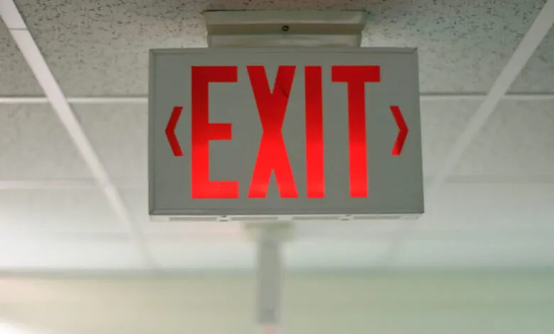 Red illuminated EXIT sign with directional arrows, hanging from a ceiling.