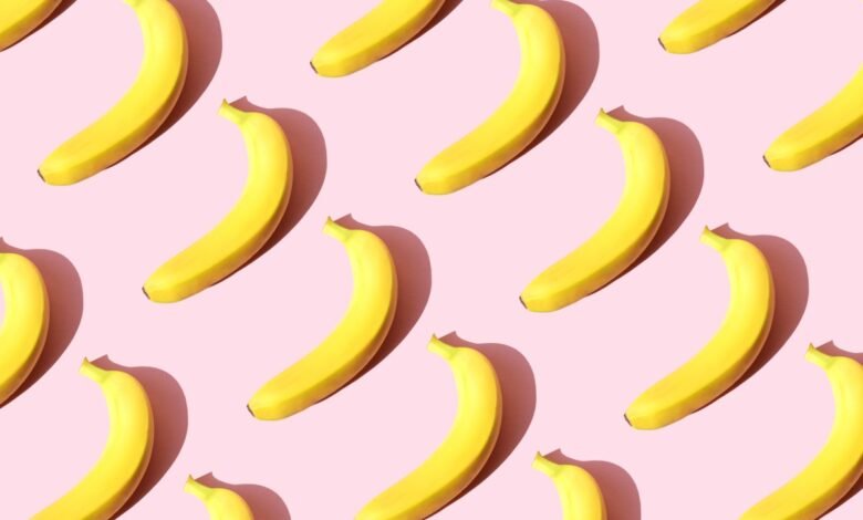 Repeating pattern of ripe yellow bananas arranged diagonally on a pink background.