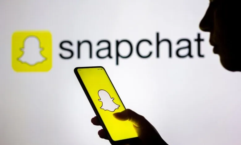 Person using Snapchat app on smartphone, Snapchat logo displayed on screen and in background.