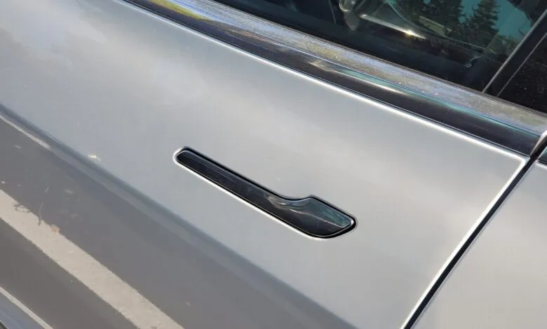 Close-up of a Tesla's flush door handle, sleek black against a silver car body.