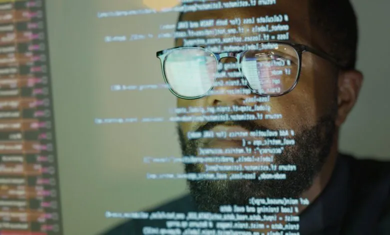 Close-up of a man's face, glasses reflecting lines of code, suggesting software development or coding.