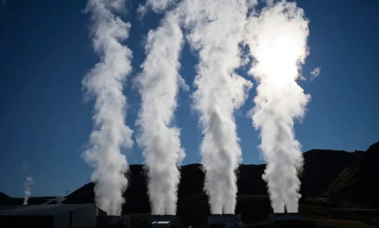 Geothermal power plant with four tall plumes of steam rising against a clear blue sky.