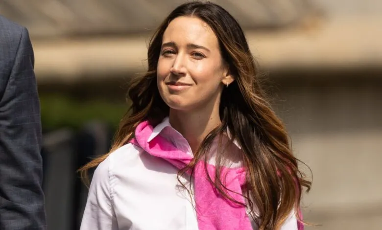 A woman with long brown hair smiles as she walks, wearing a white shirt and pink scarf.