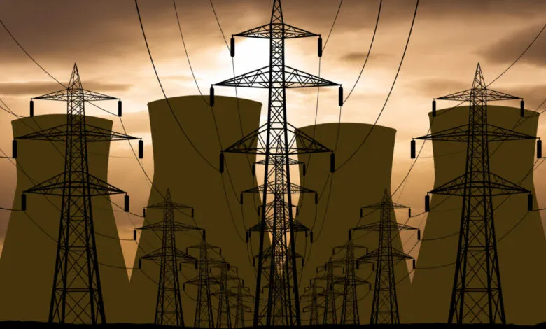 Silhouetted nuclear power plant cooling towers and high-voltage power lines at sunset.