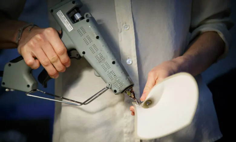 Close-up of hands using a hot glue gun to assemble a paper flower.
