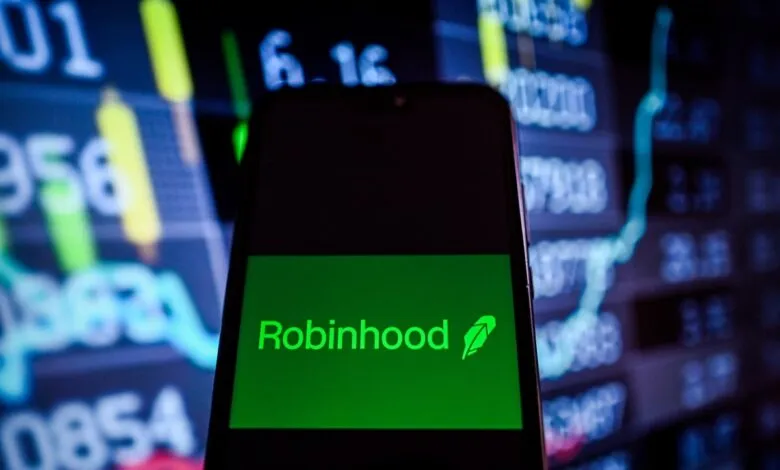 Robinhood app logo displayed on a smartphone against a blurred background of stock market data.