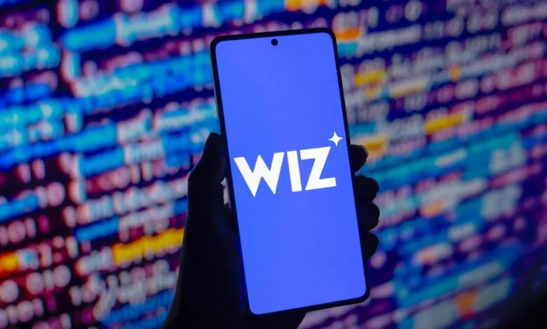 Hand holding a smartphone displaying the Wiz logo against a blurred background of code.