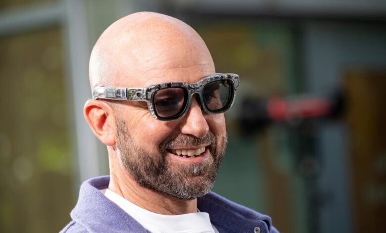 Close-up of a smiling bald man wearing distinctive tech glasses.