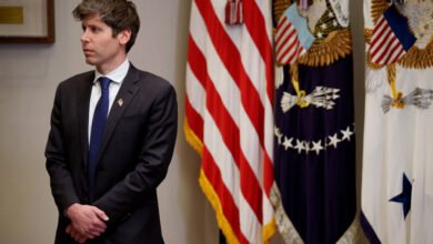 Sam Altman, OpenAI CEO, stands in a formal setting with American flags in the background.