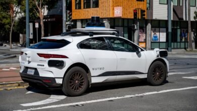 A Waymo self-driving Jaguar I-PACE, equipped with sensors, navigates a city street.
