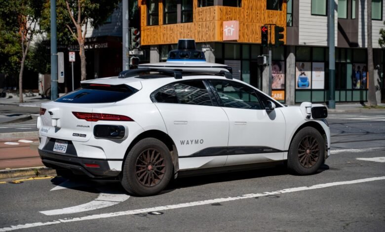 A Waymo self-driving Jaguar I-PACE, equipped with sensors, navigates a city street.
