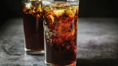 Two tall glasses filled with dark cola and ice cubes, showing effervescence.