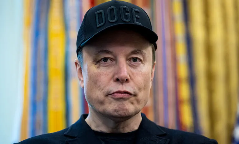 Close-up of Elon Musk wearing a black hat with 'DOGE' on it.