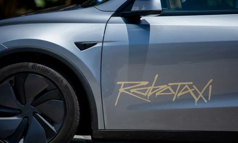 Close-up of a silver Tesla with a gold 'RoboTaxi' decal on the side.