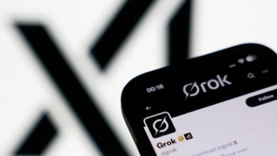 Close-up of a smartphone displaying the Grok app and Twitter profile, featuring the Grok logo and account details against a blurred background.
