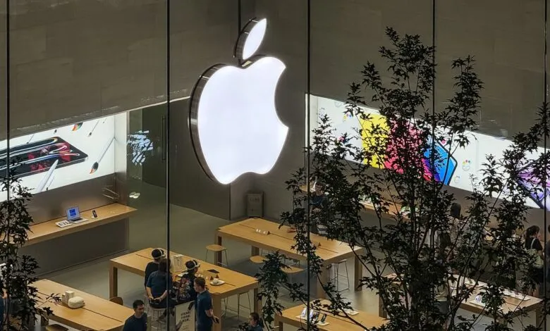 Illuminated Apple logo above a bustling Apple Store, seen from an upper level.