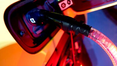 Close-up of an electric vehicle charging port with a cable plugged in, illuminated in red and orange light.