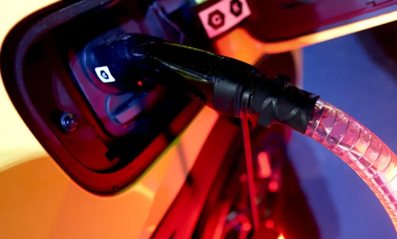 Close-up of an electric vehicle charging port with a cable plugged in, illuminated in red and orange light.